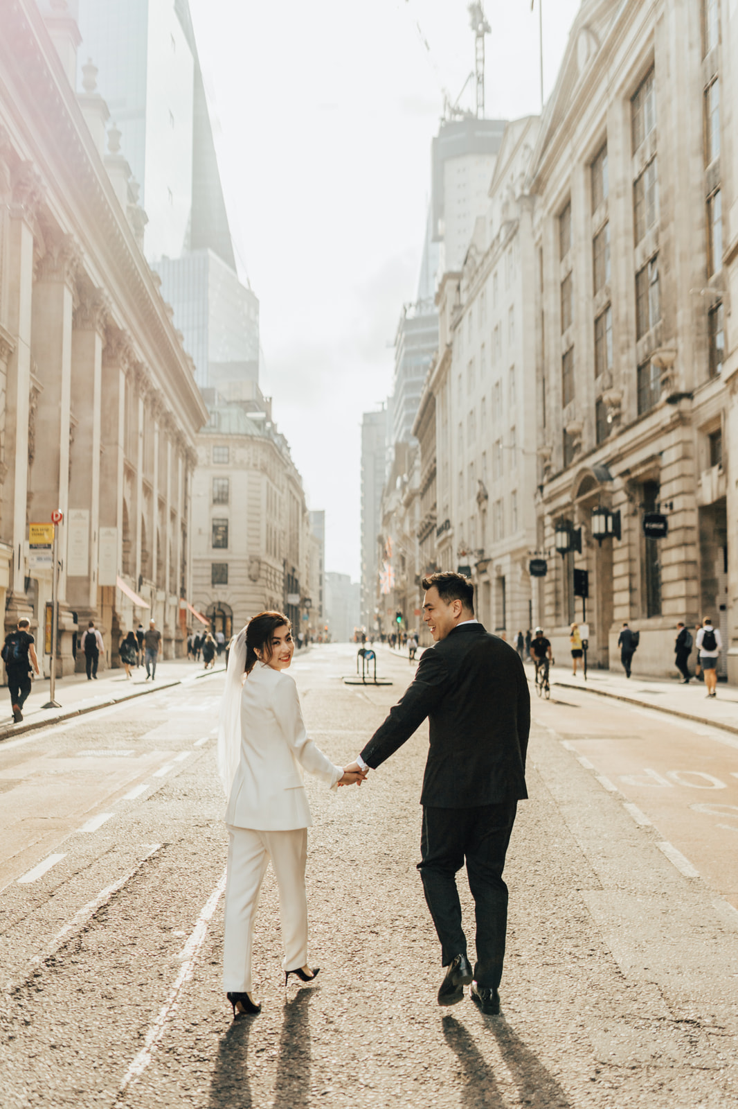 Man and Woman holding hands in the streets of london with no traffic looking over their shoulder