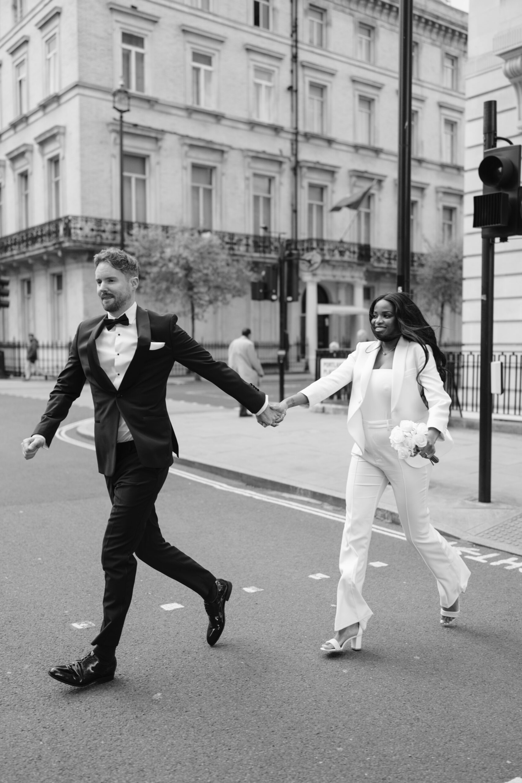 black and white photo of bride and groom running across the road