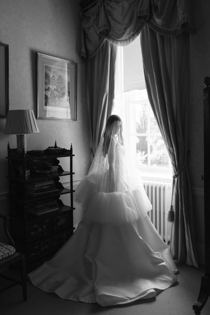 black and white photo of bride at the window wearing veil