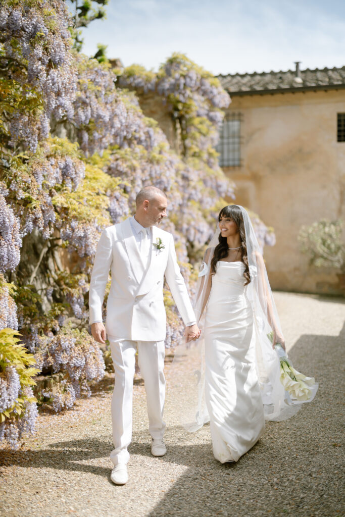 bride and groom walking holding hands infront of wisteria at Villa cetinale