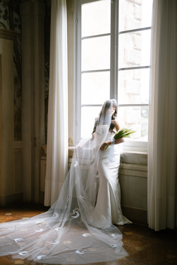 bride standing in front of window wearing moon veil