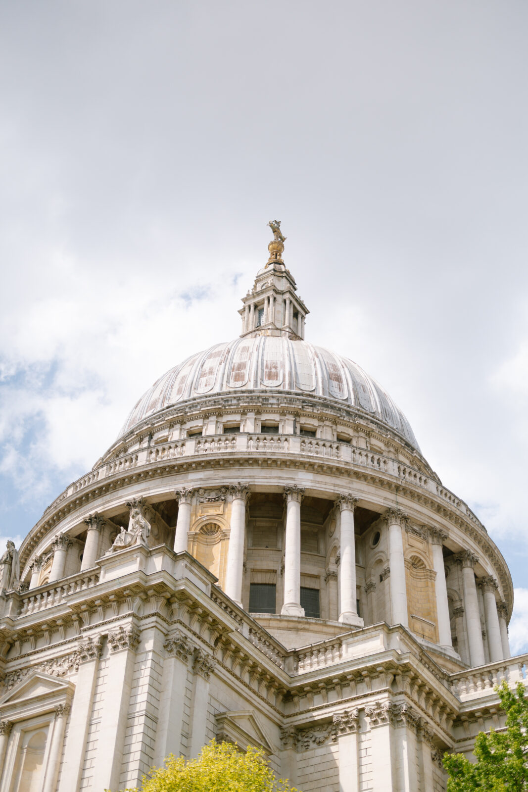 A low-angle view of the dome of St. Paul’s Cathedral in London, featuring classical columns and ornate architectural details under a cloudy sky.