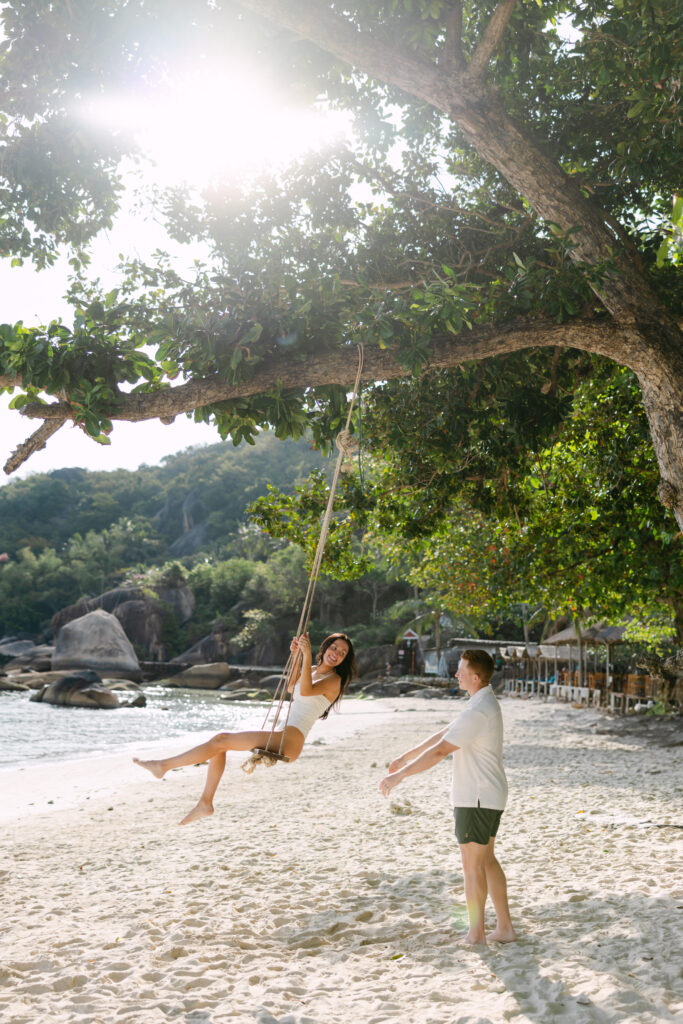 A man and woman on a swing on a beach.