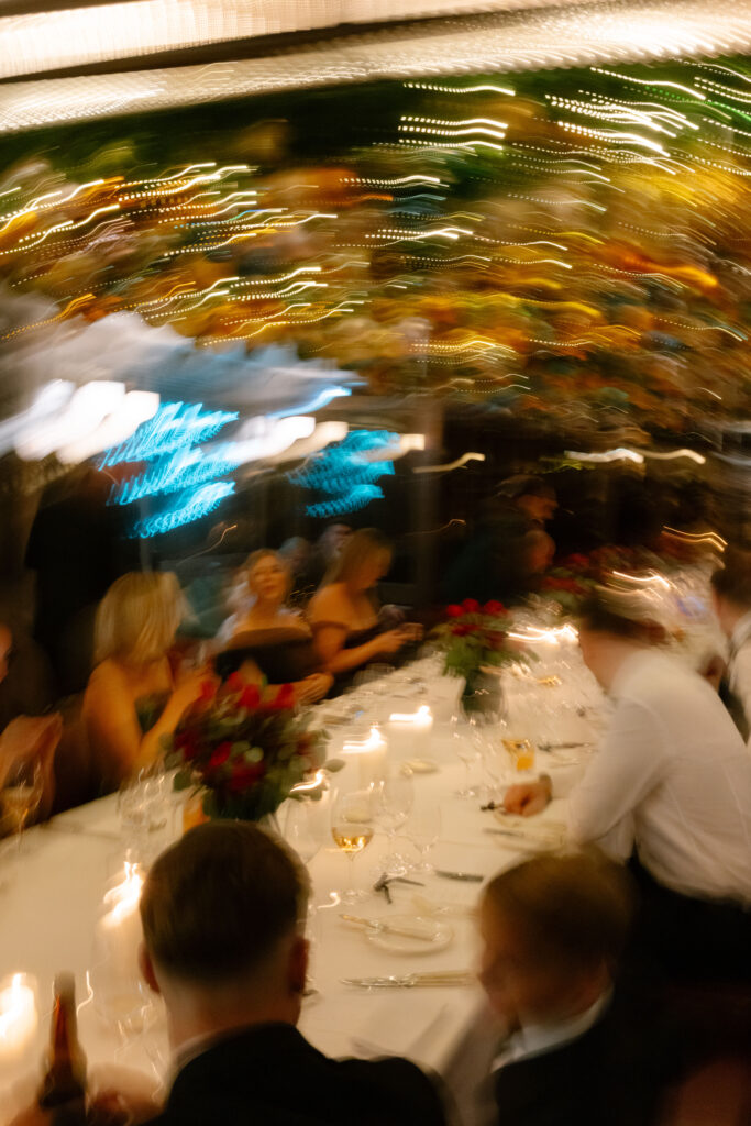 A blurred, swirling image shows people seated around a decorated dinner table with flowers and candles, under warm, festive lights, creating a dynamic and energetic atmosphere.