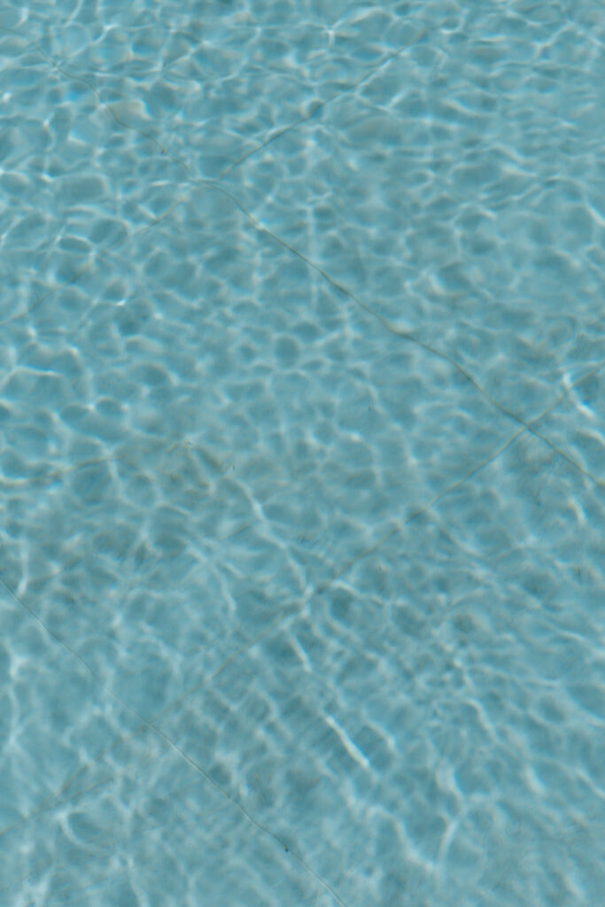 Clear blue water with sunlight creating rippling patterns on the surface and visible tile lines beneath.
