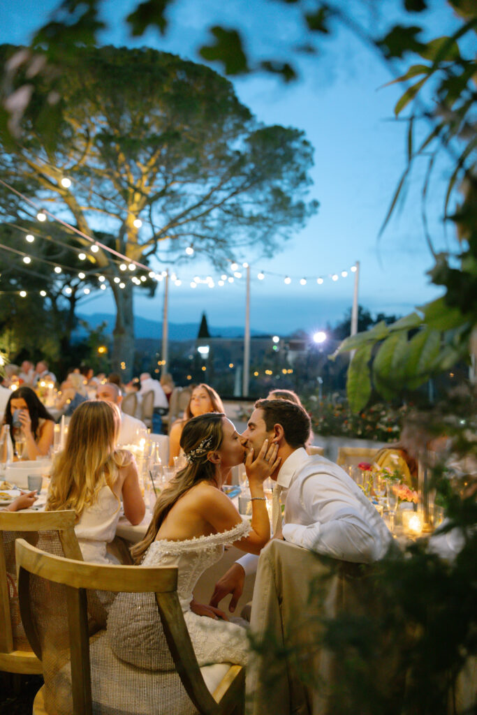 A man and woman kissing at a table.